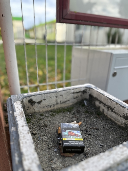 un paquet de cigarettes laissé avec les mégots dans un bac devant l'école